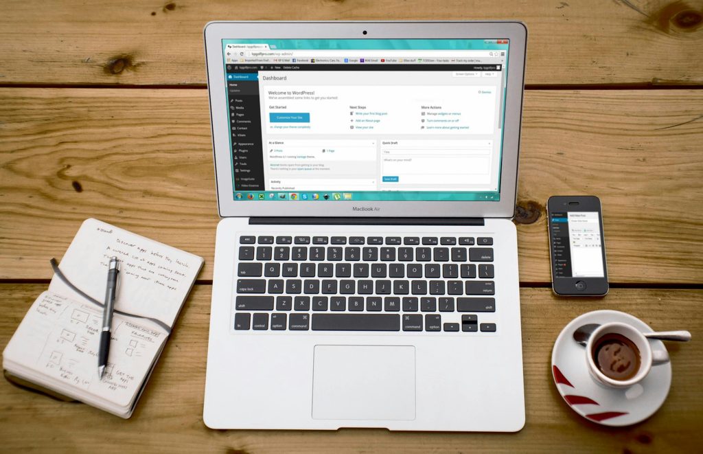 Turned-on Macbook Air Beside Black Iphone 4, Cup of Tea, and Notebook on Brown Wooden Surface
